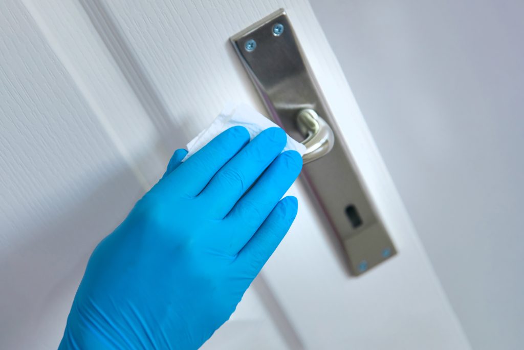 A blue plastic gloved hand cleans a metal door handle